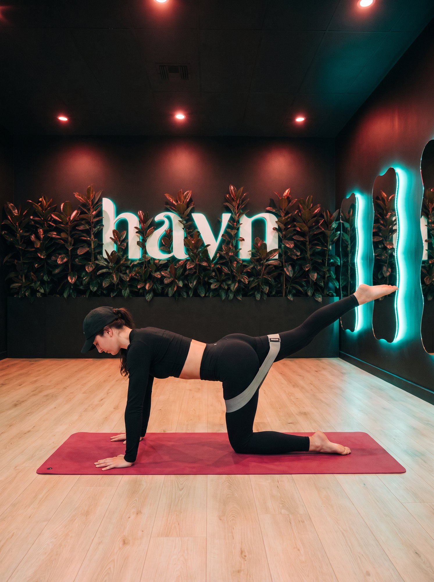 BrieAnna on a raspberry mat at havn fit, lifting one leg with a band around her thighs